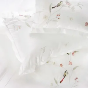 Overhead view of white pillowcases with embroidered birds and floral branches.