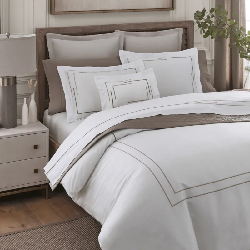 Home Treasures Corso white quilted coverlet with taupe embroidered border on styled bed.