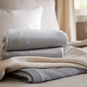 SDH Gobi matelasse blankets in silver and champagne stacked on a bed.